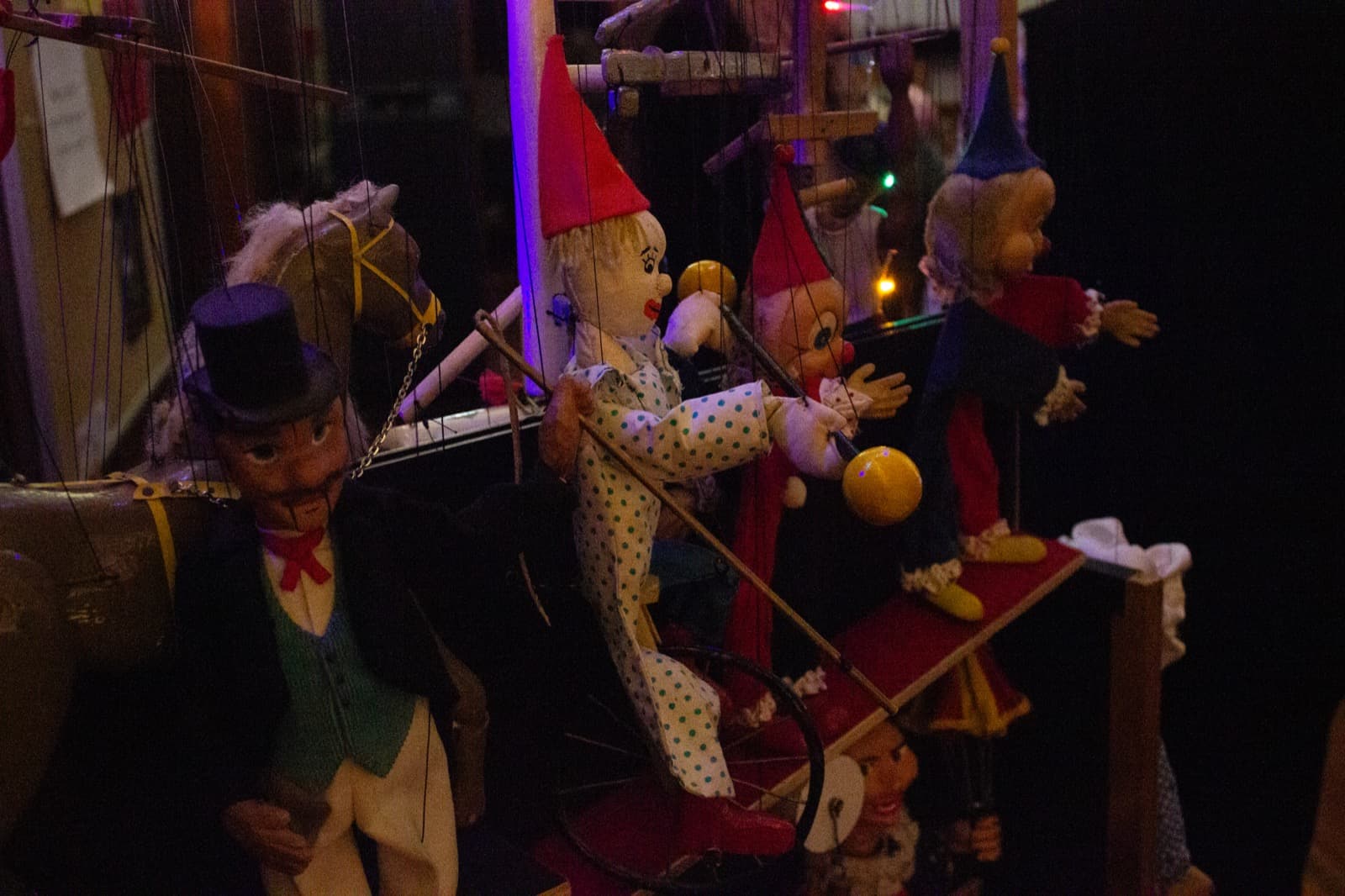 a display of antique marionettes on a shelf including a clown on a unicycle a man in a top hat and waistcoat and a two clowns in red and blue costumes